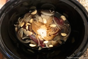 beef and sliced onions in bowl of slow cooker