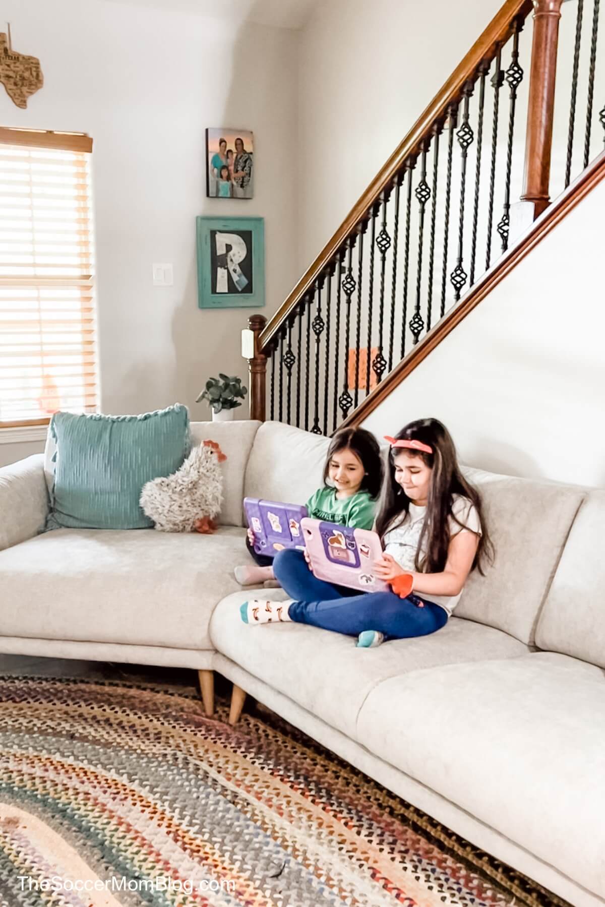 two little girls sitting on a couch playing with tablets