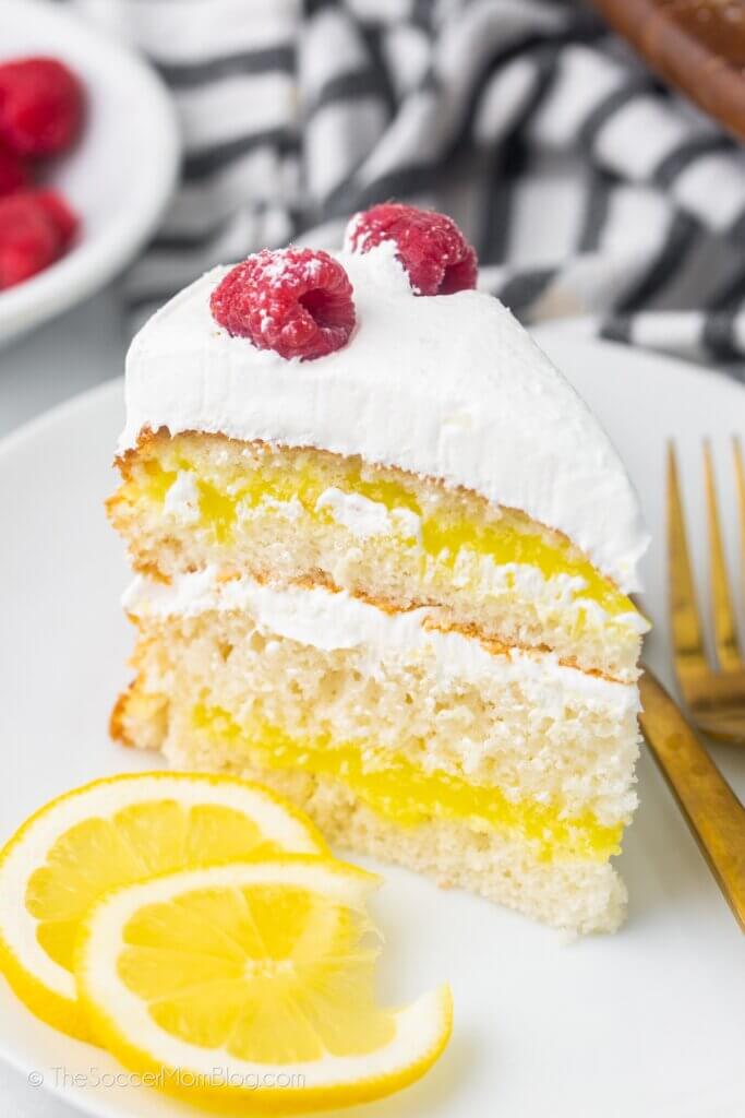 slice of lemon layer cake, topped with whipped cream and raspberries