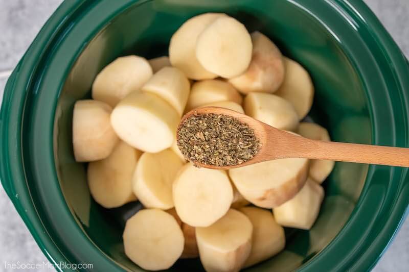 chopped potatoes in slow cooker with spoonful of herbs