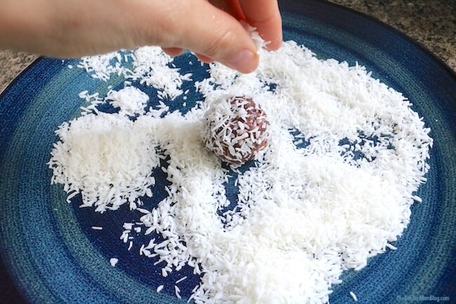 rolling a homemade chocolate protein ball in shredded coconut