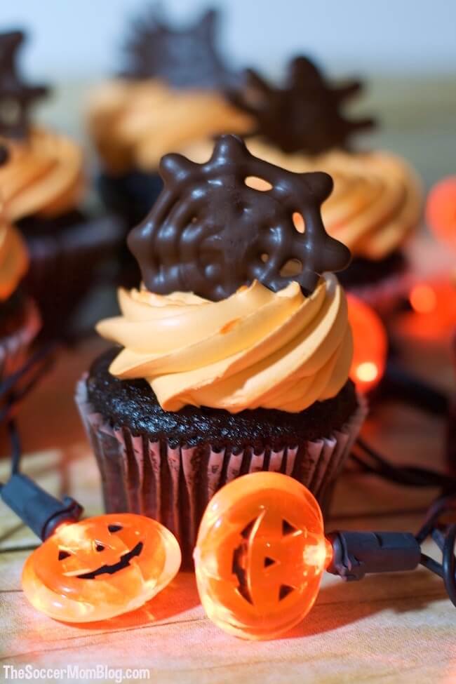 Spider web cupcakes close-up with glowing pumpkin lights