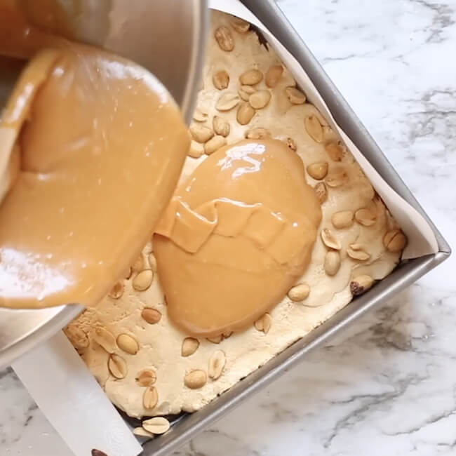 pouring melted caramel into baking pan with peanut nougat