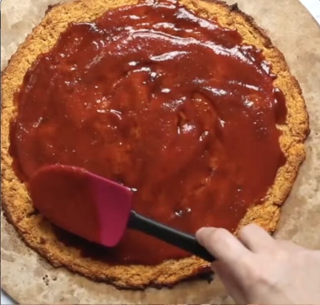 spreading tomato sauce on sweet potato pizza crust