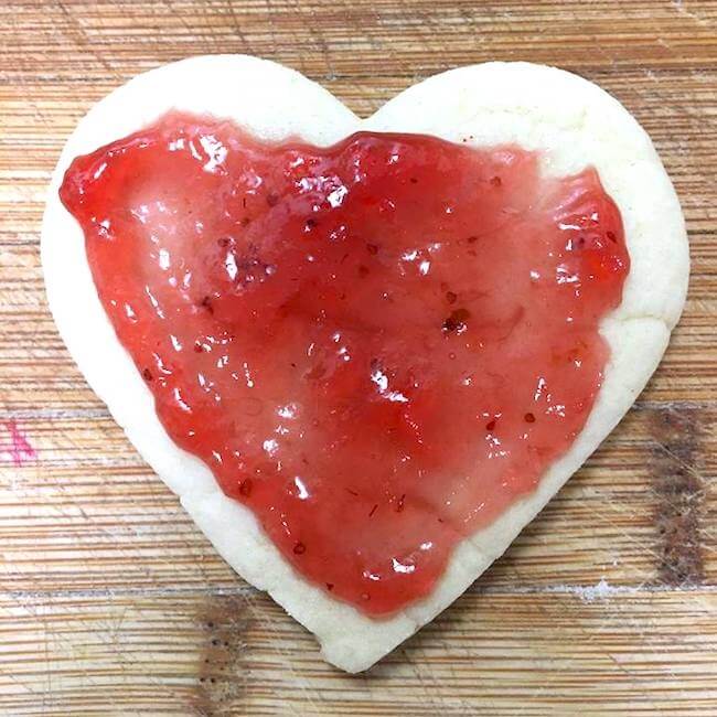 These stained glass heart cookies make an absolutely gorgeous Valentine's Day treat! Real from-scratch sugar cookies with sparkling pink icing and a jelly "stained glass" cutout center.