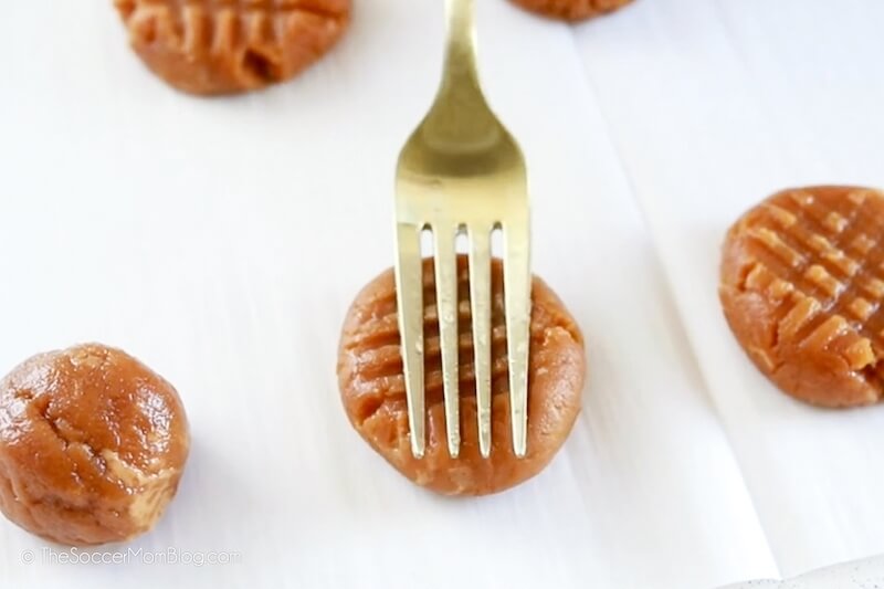 pressing peanut butter cookies with a fork to make a criss-cross pattern