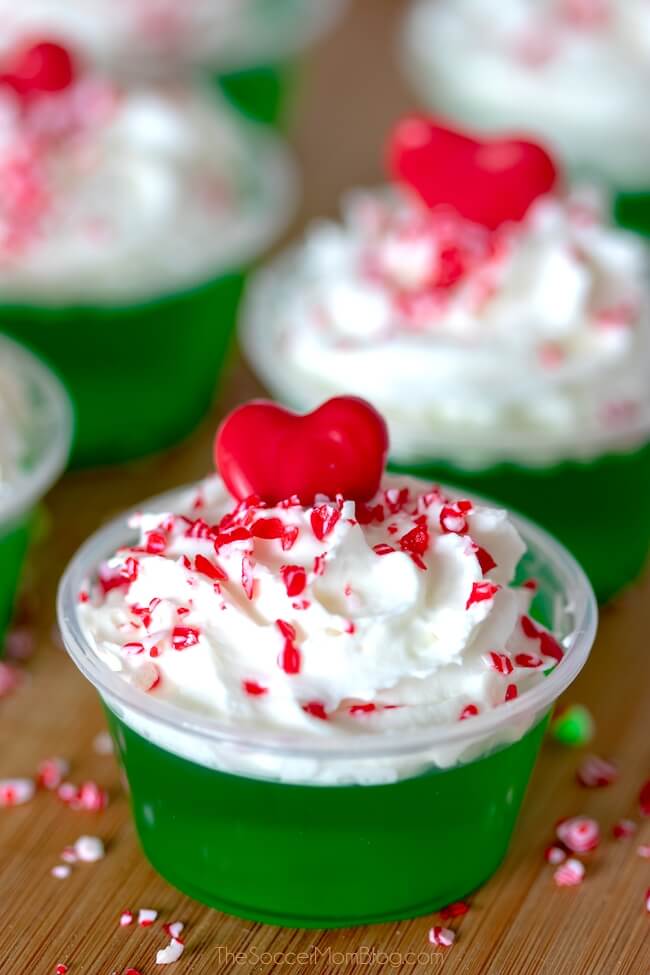 green Grinch inspired jello shots with whipped cream and red heart on top