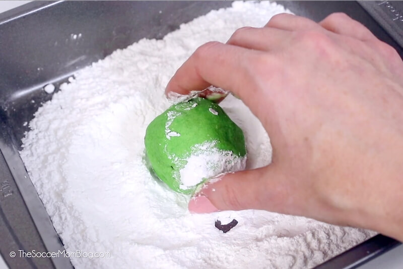 rolling a ball of green cookie dough in powdered sugar