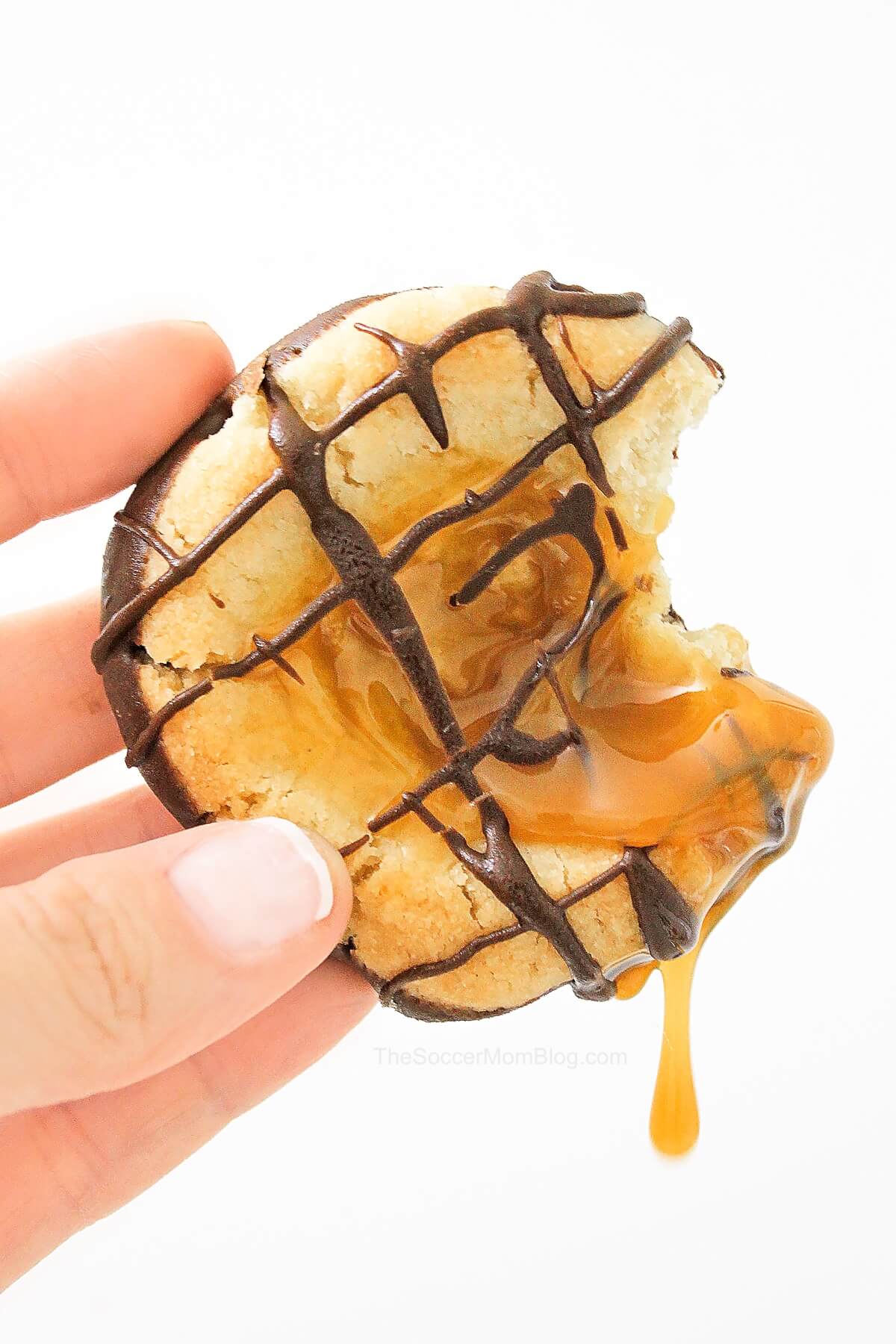 holding a caramel filled cookie with caramel drips.