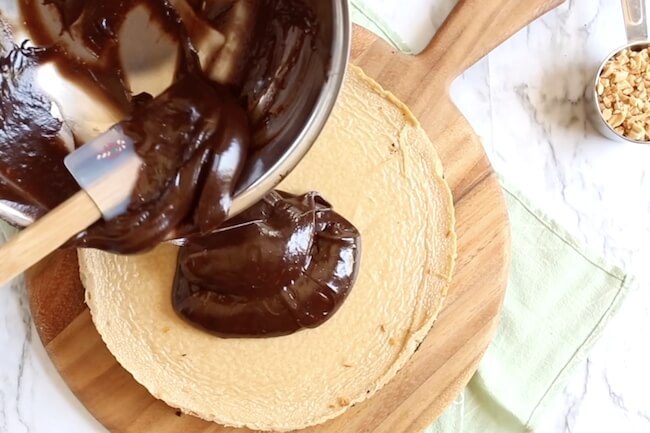 spreading chocolate ganache on top of peanut butter cheesecake