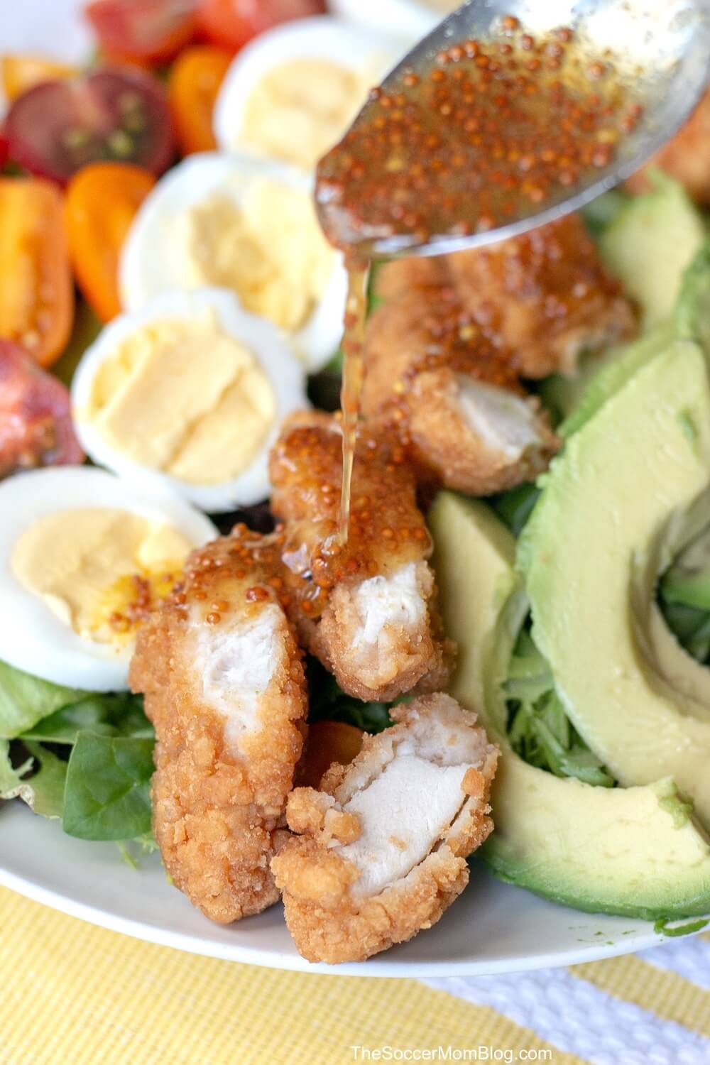 drizzling honey mustard on a Cobb salad with fried chicken