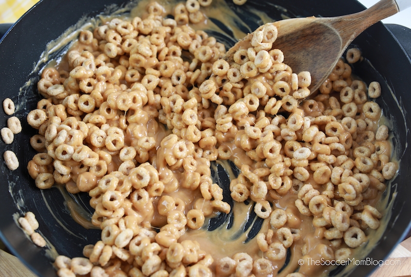 stirring cheerios into melted peanut butter to make cereal treats
