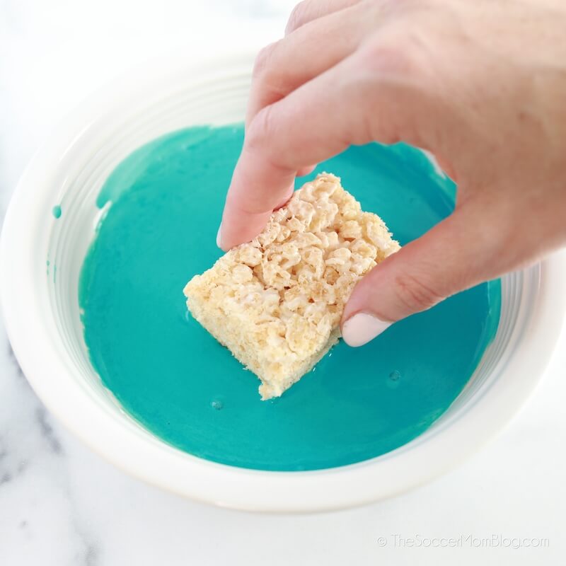 dipping rice krispie treat into blue royal icing