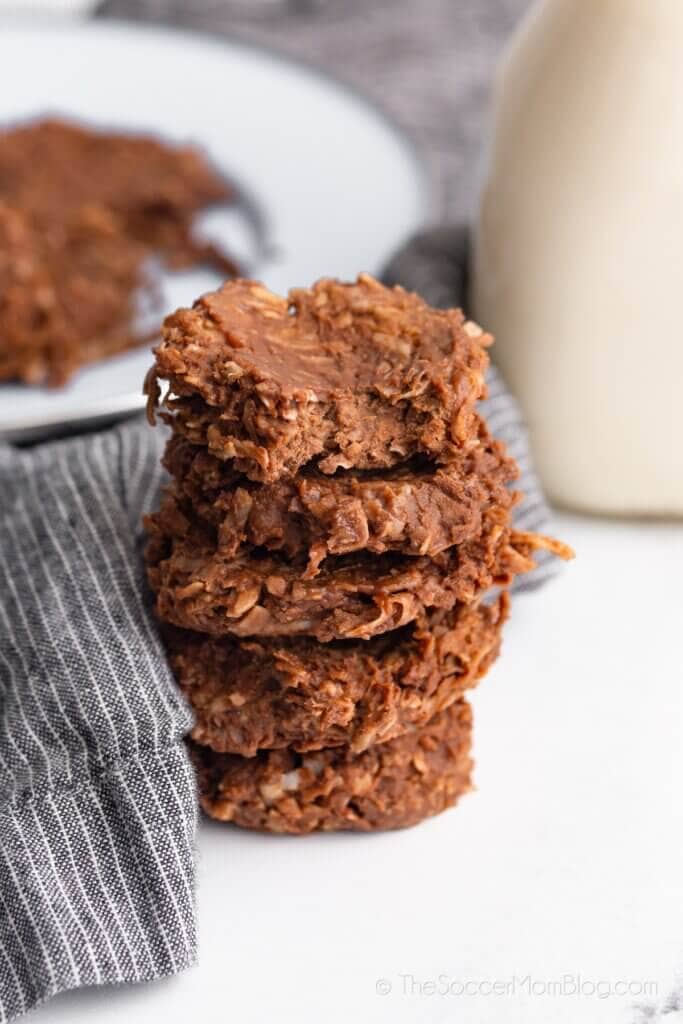 stack of chocolate no bake cookies with plate and milk in background