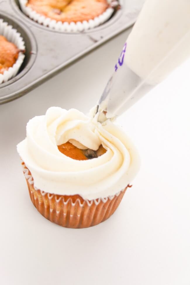 piping cinnamon vanilla frosting onto cupcake
