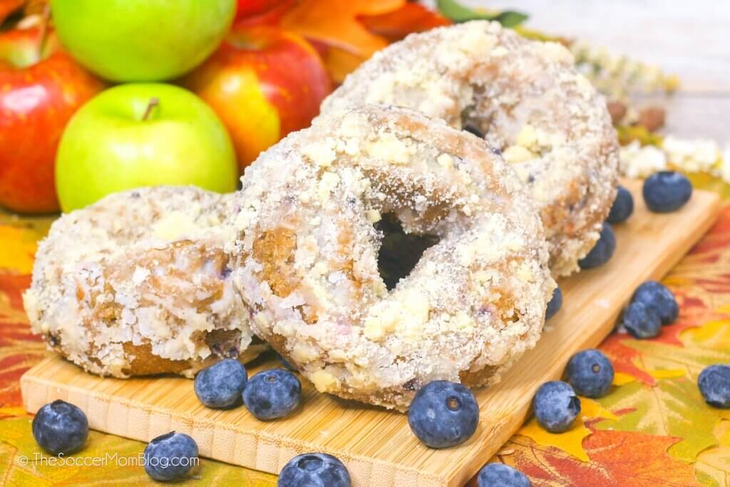 Apple Blueberry Donuts piled on a serving board surrounded by fresh fruit