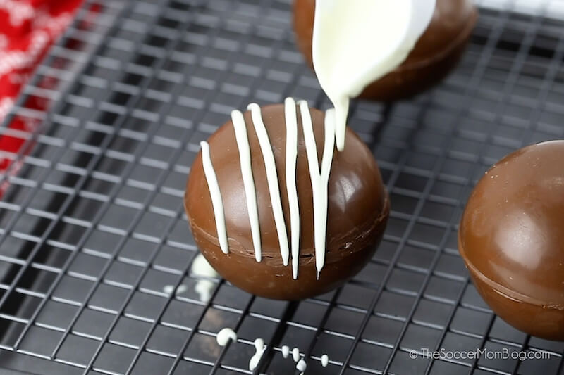 drizzling white chocolate on top of a hot cocoa bomb