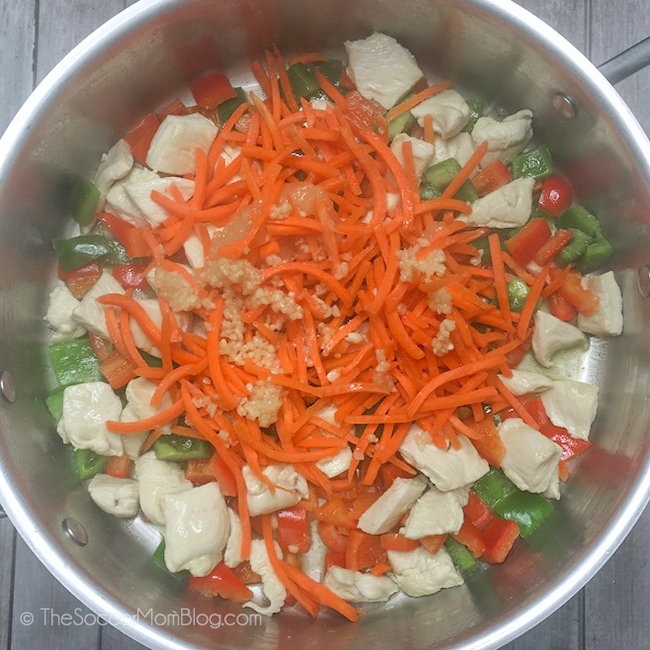 chicken, peppers, carrots, and minced garlic cooking in pan