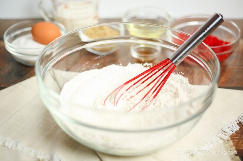 glass mixing bowl with baking flour and wire whisk