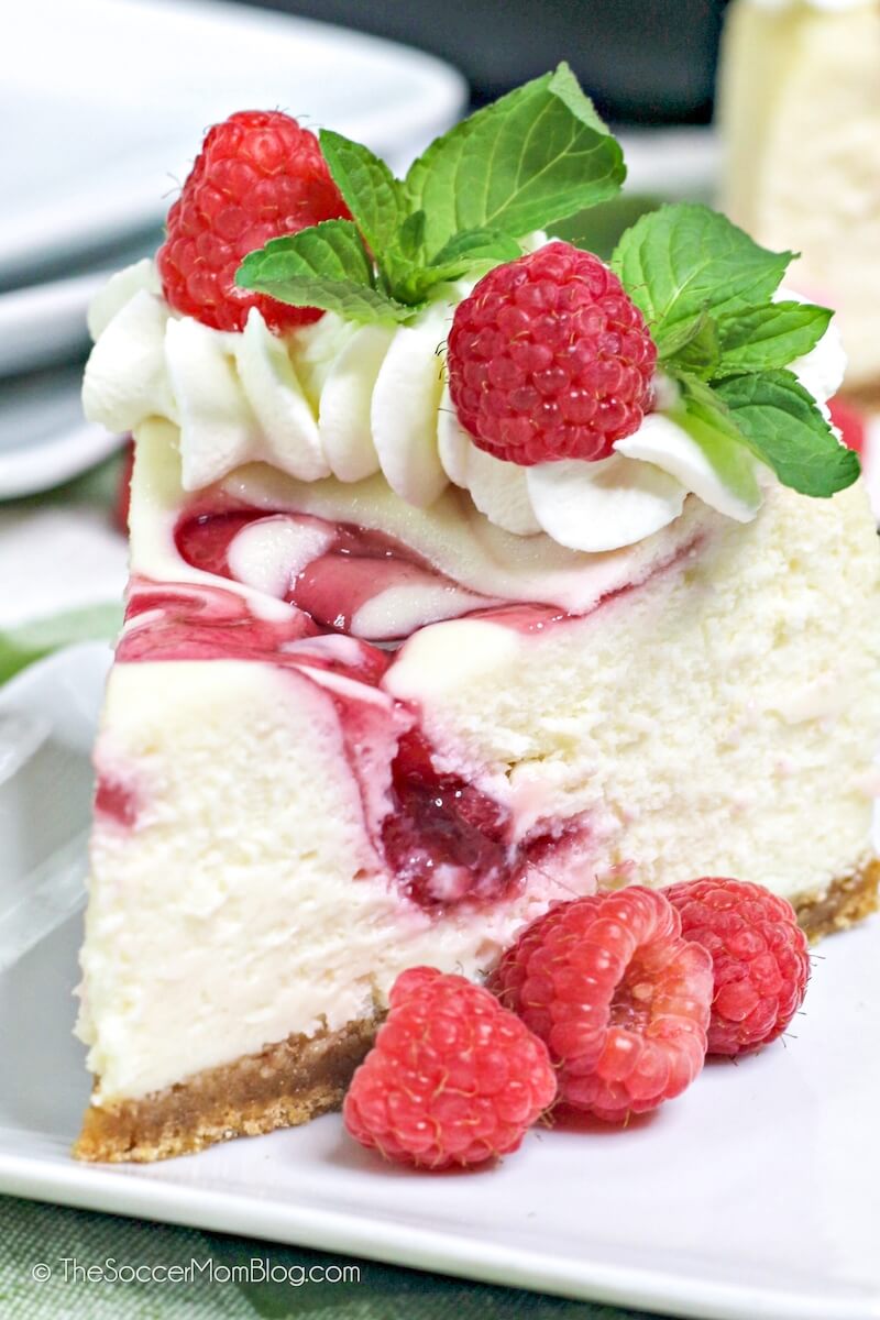 Close up of a slice of raspberry swirl cheesecake with mint and fresh berries