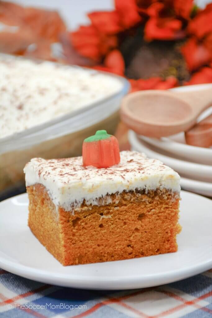 slice of pumpkin sheet cake topped with cream cheese frosting and candy pumpkin