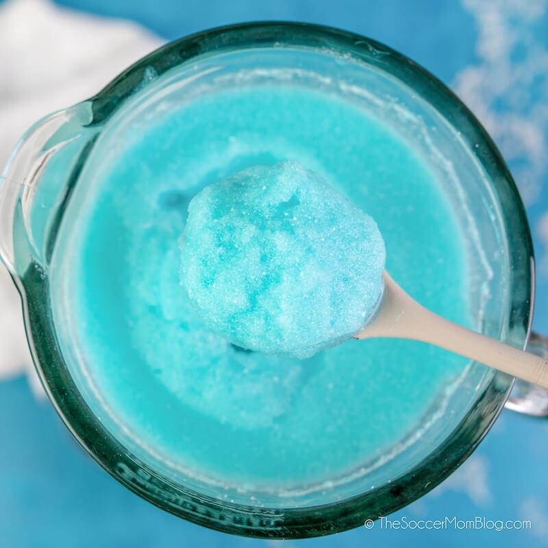stirring an icy blue drink with wooden spoon, in a blender