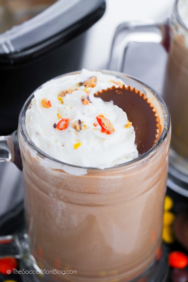 close up of a clear mug of hot chocolate with crushed Reese's Pieces on top