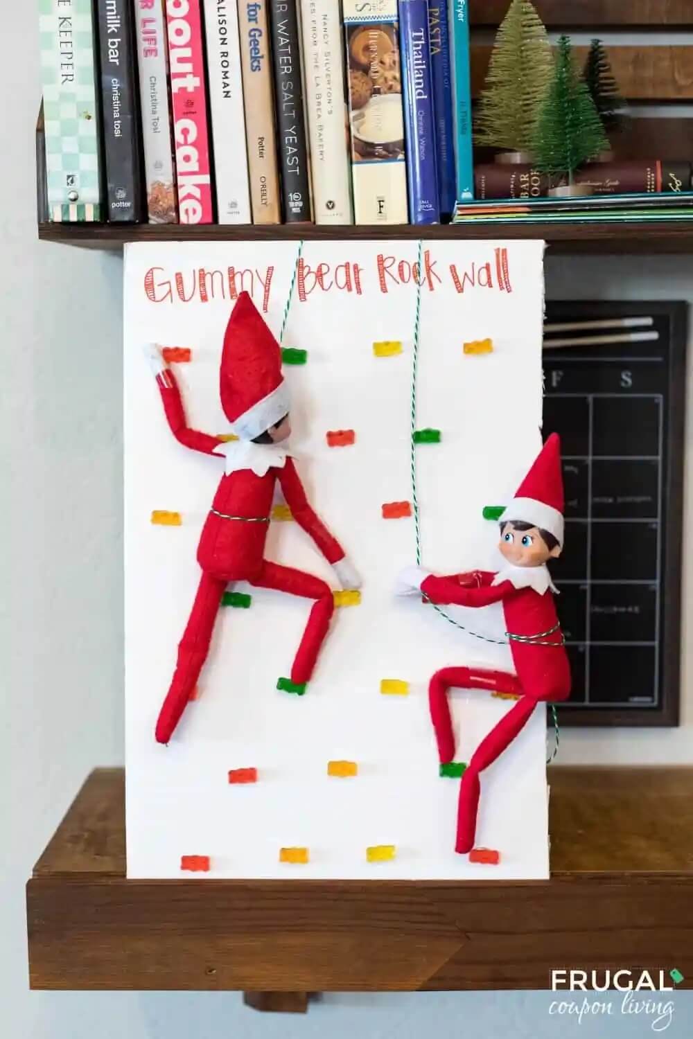 two Elf on the Shelf dolls "rock climbing" on a piece of cardboard with gummy bear footholds.