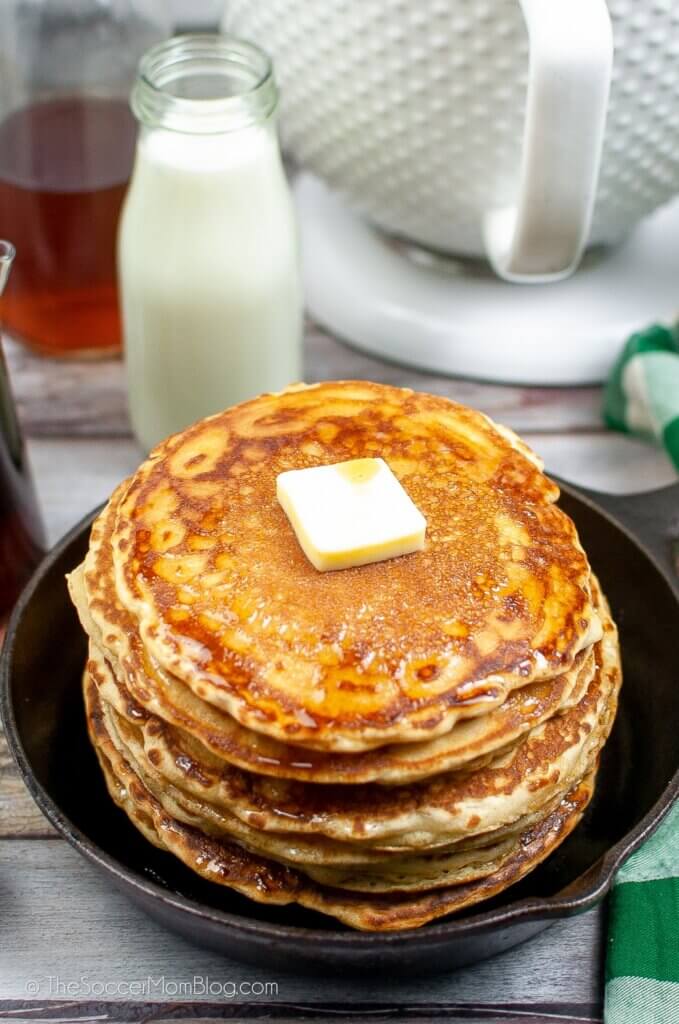 A stack of Sourdough Pancakes in a cast iron skillet, topped with butter