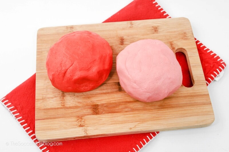 a ball of red cookie dough and a ball of pink cookie dough on a cutting board