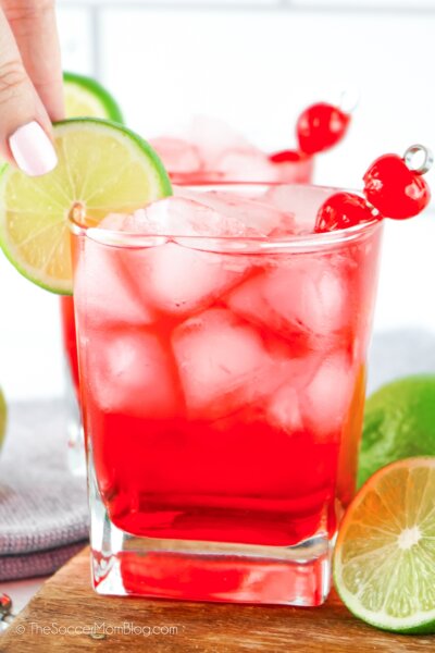 Placing a lime wheel on the rim of a bright red Dirty Shirley Temple cocktail