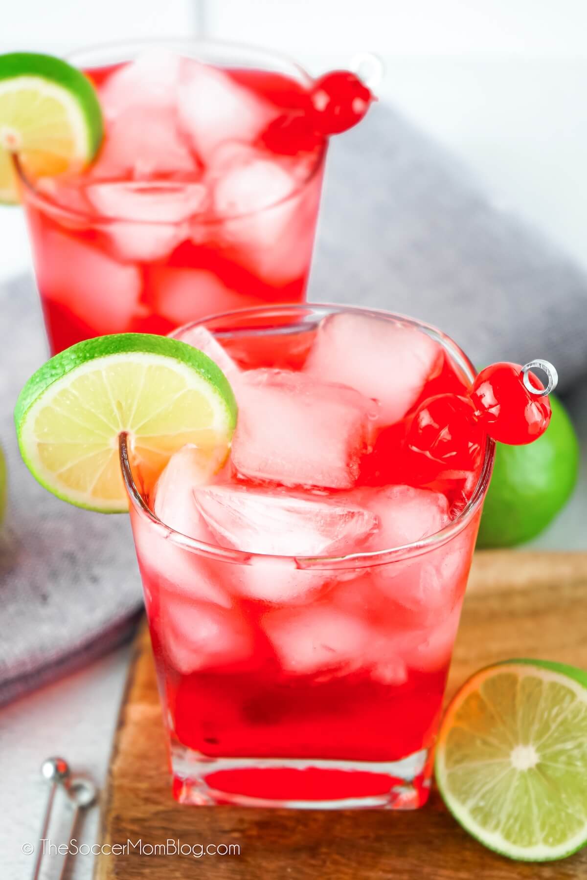 two bright red cocktails with cherries and lime