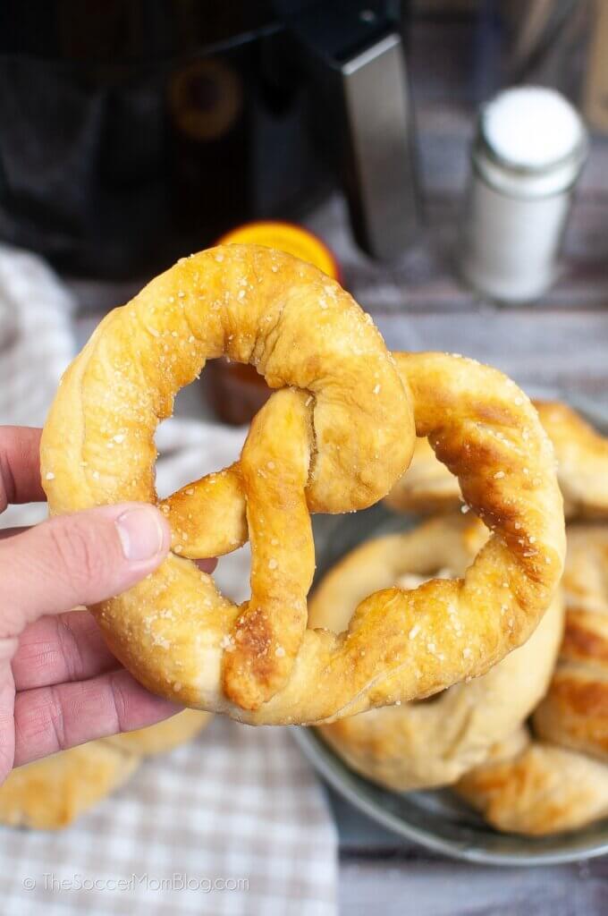 hand holding a large homemade soft pretzel in front of an air fryer