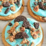 big chocolate chip cookie decorated with blue frosting and cookie crumbles