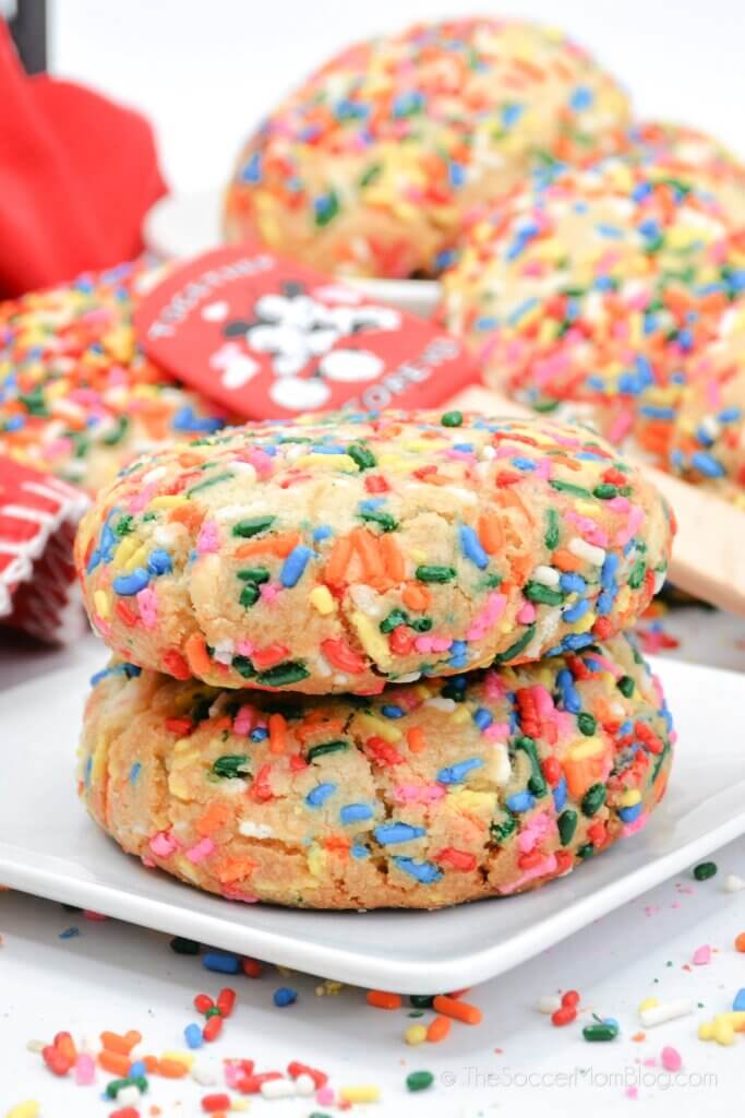 two funfetti cookies stacked on plate, surrounded by sprinkles