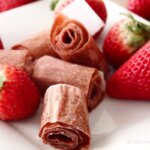 homemade fruit roll-ups with fresh strawberries on plate.