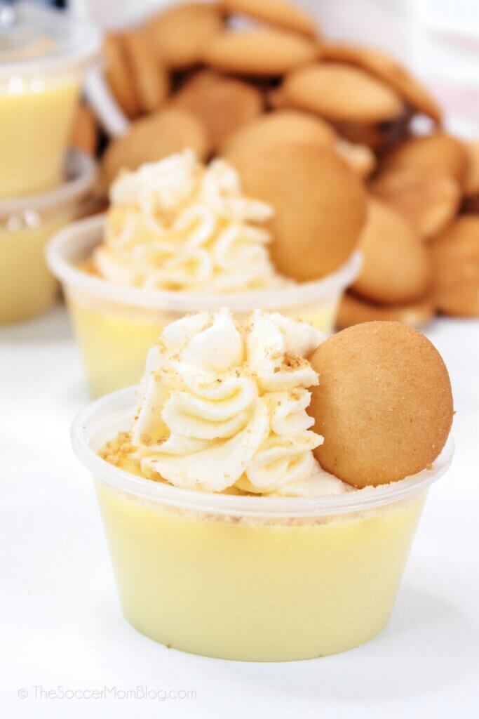 small plastic shot cups filled with banana pudding and topped with whipped cream and cookie