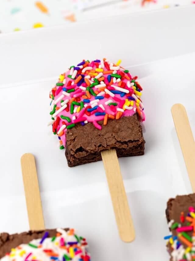 close up of a brownie decorated to look like a popsicle with pink candy coating and a popsicle stick.