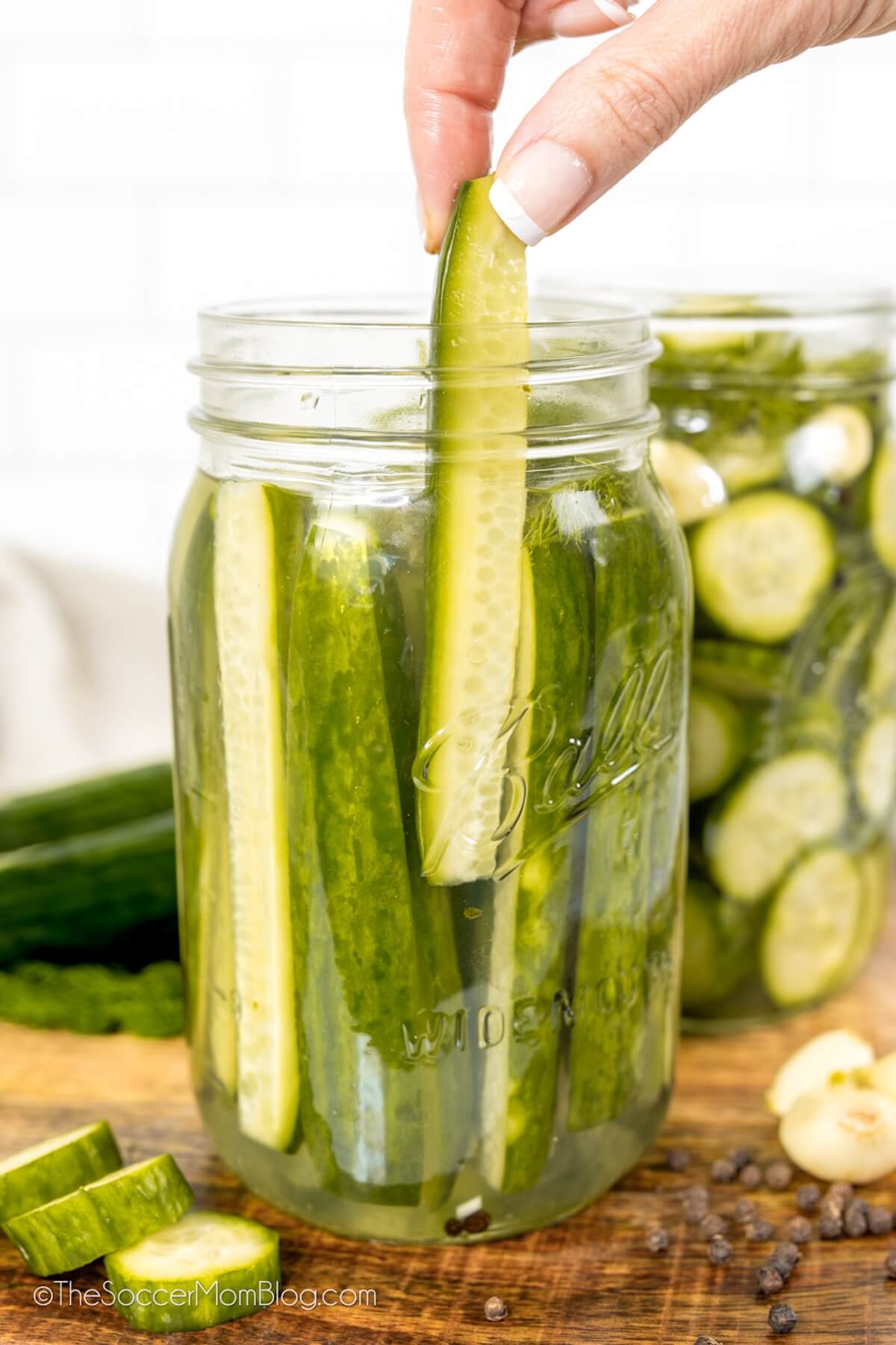 pulling a pickle spear out of a mason jar of homemade dill pickles
