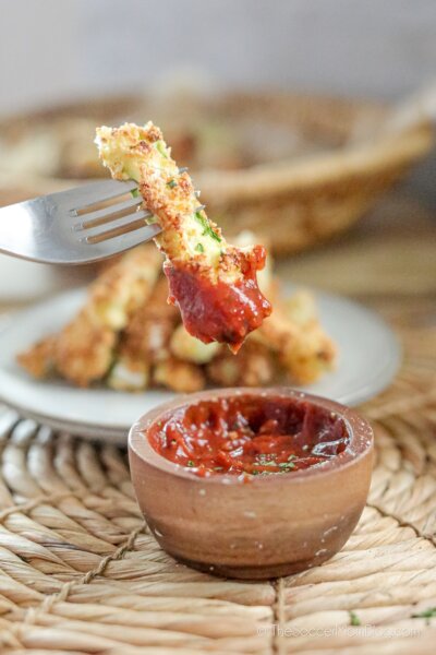 dipping a crispy zucchini fry in ketchup