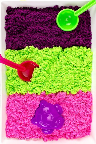 play tray with 3 colors of homemade kinetic sand: purple, green, and pink - close up