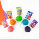 balls of playdough arranged in a rainbow, next to packets of Kool Aid