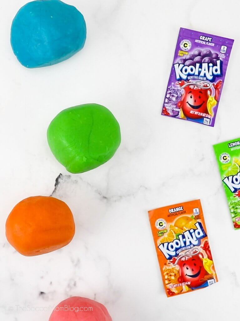 balls of colorful playdough next to Kool Aid packets