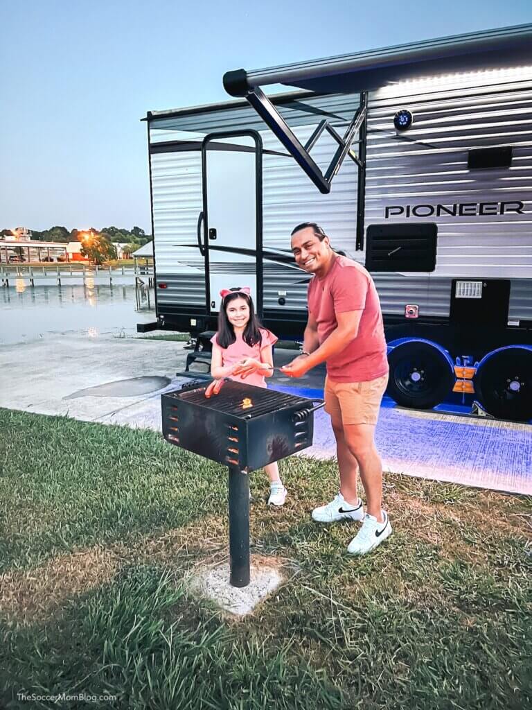 dad and daughter roasting hot dogs in front on RV