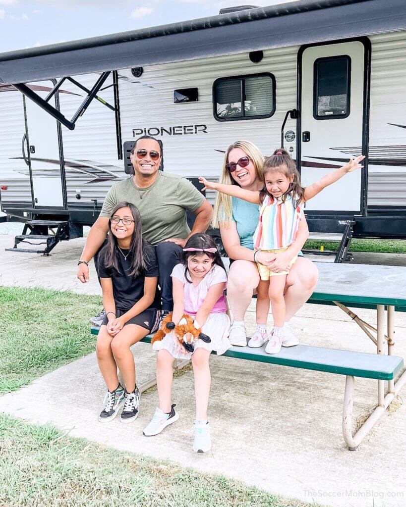 family sitting on a picnic table in front of a recreational vehicle
