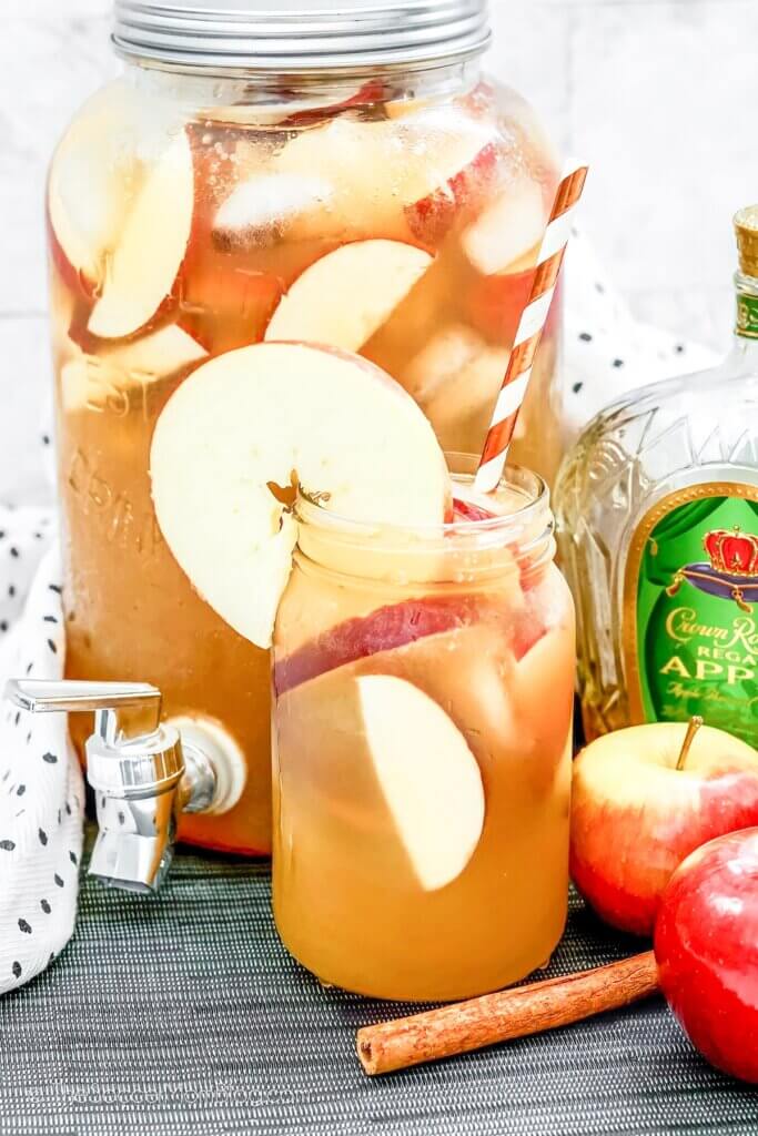 A large spouted pitcher filled with golden whiskey punch and apple slices