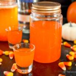two mason jars filled with homemade candy corn moonshine, surrounded by candy and pumpkins