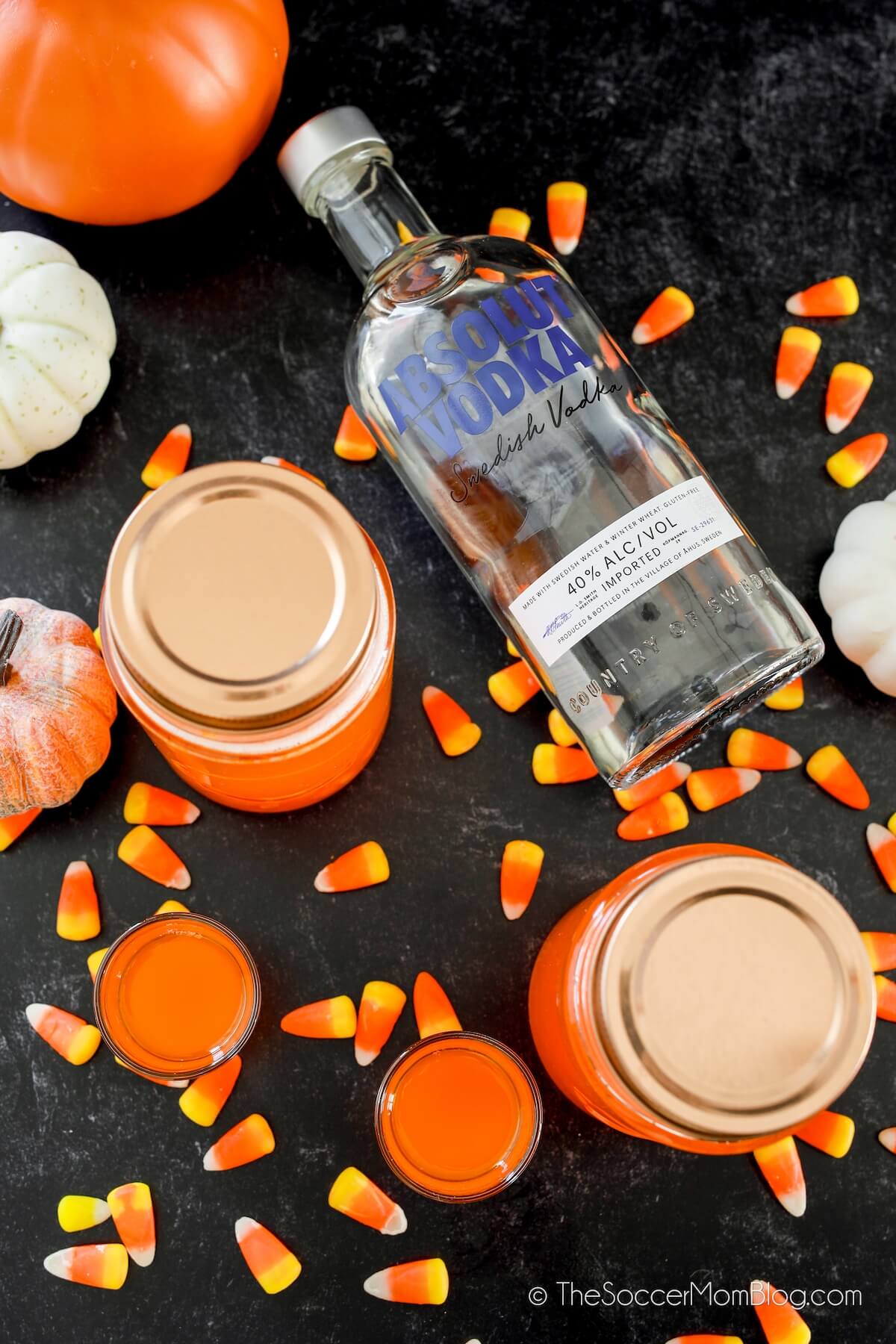 flat lay photo of jars of homemade moonshine, candy corn, Absolut vodka bottle