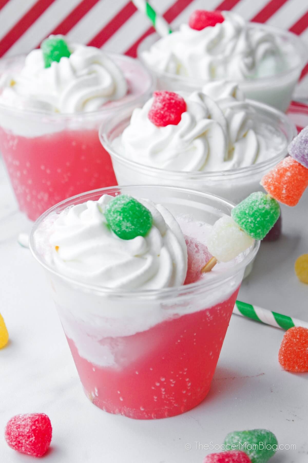cups with colorful Christmas punch topped with whipped cream and gumdrops