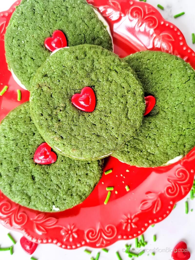 A plate of Grinch Cookie Sandwiches (green with a red heart sprinkle on top)